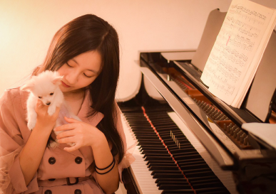 女性がピアノの前の椅子に座りながら白い子犬を愛でている様子