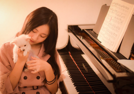 女性がピアノの前の椅子に座りながら白い子犬を愛でている様子